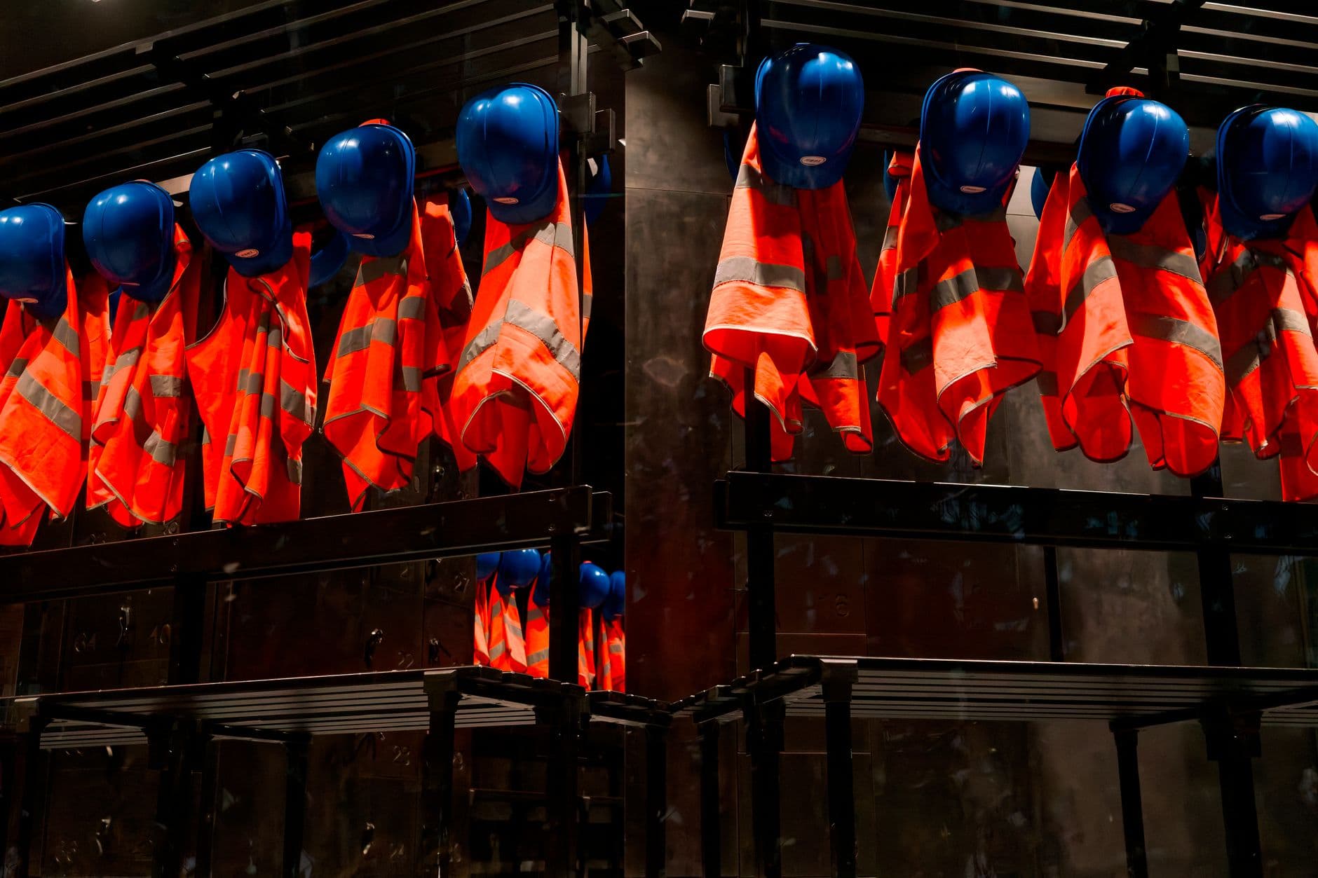 Reflective Tape — Row of orange safety vests and blue helmets hanging in industrial setting