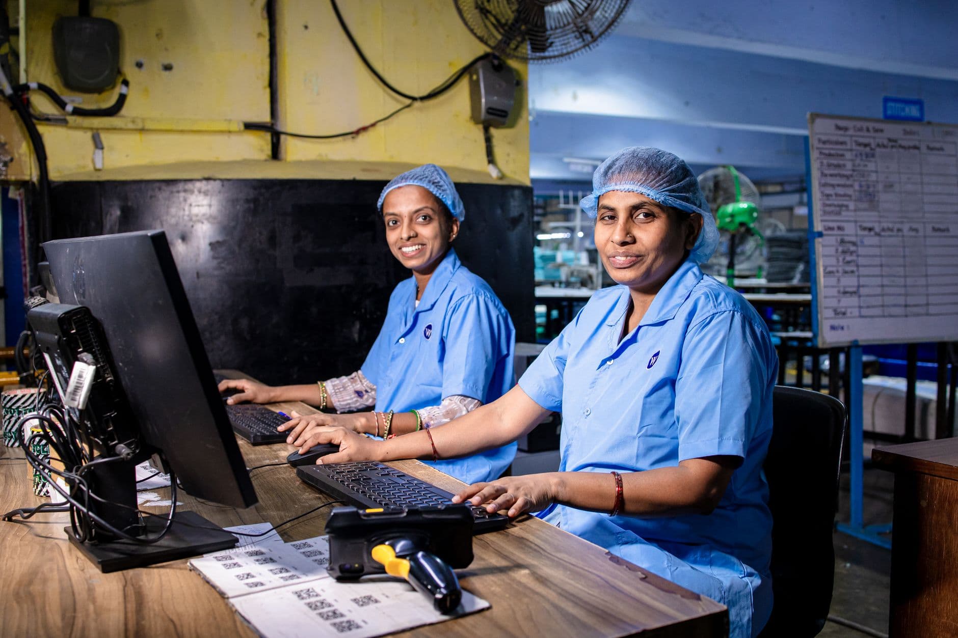 Two female workers at a textile factory operating computers in an industrial setting.
